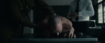 Movie still from “The Courier” (2020), directed by Dominic Cooke – A man with a shaved head is lying on a table; Medium shot, Low angle