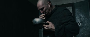 Movie still from “The Courier” (2020), directed by Dominic Cooke – A bald man in a black shirt is holding a metal bowl; Close Up shot, High angle