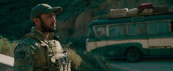 Movie still from “The Covenant” (2023), directed by Guy Ritchie – A man in a military uniform standing in front of a truck; Medium shot, Over the shoulder angle