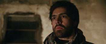 Movie still from “The Covenant” (2023), directed by Guy Ritchie – A man with a goatee and a beard looking into the distance; Close Up shot, Low angle