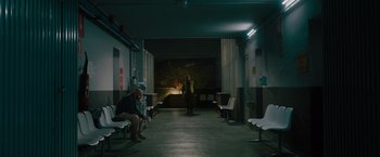 Movie still from “The Covenant” (2023), directed by Guy Ritchie – Two people sitting in a room with a man standing in the background; Wide shot, High angle