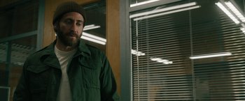 Movie still from “The Covenant” (2023), directed by Guy Ritchie – A man standing in front of a window with blinds; Medium shot, Over the shoulder angle