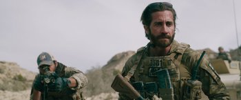 Movie still from “The Covenant” (2023), directed by Guy Ritchie – A person holding a gun; Medium shot, Over the shoulder angle