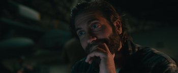 Movie still from “The Covenant” (2023), directed by Guy Ritchie – A man with a beard is sitting in a dark room; Close Up shot, Over the shoulder angle