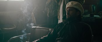 Movie still from “The Covenant” (2023), directed by Guy Ritchie – A man sitting in a chair with a cigarette in his mouth; Medium shot, Low angle