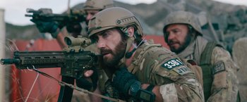 Movie still from “The Covenant” (2023), directed by Guy Ritchie – A man with a beard wearing a helmet and holding a rifle; Medium shot, Over the shoulder angle