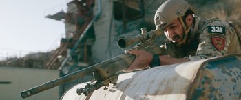 Movie still from “The Covenant” (2023), directed by Guy Ritchie – A man with a rifle aiming at a building; Medium shot, Low angle