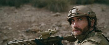 Movie still from “The Covenant” (2023), directed by Guy Ritchie – A man with a helmet on and a rifle in his hand; Close Up shot, Over the shoulder angle