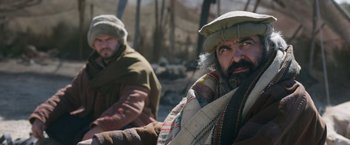 Movie still from “The Covenant” (2023), directed by Guy Ritchie – A man with a beard wearing a hat and a scarf; Medium shot, Over the shoulder angle