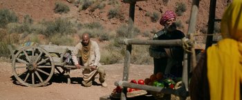 Movie still from “The Covenant” (2023), directed by Guy Ritchie – A man kneeling down next to a table of vegetables; Wide shot, Over the shoulder angle