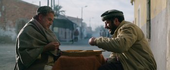 Movie still from “The Covenant” (2023), directed by Guy Ritchie – Two men sitting at a table with a plate of food in front of them; Medium shot, Low angle