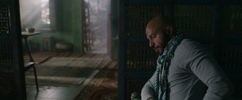 Movie still from “The Covenant” (2023), directed by Guy Ritchie – A bald man sitting in a chair in a living room; Medium shot, Over the shoulder angle