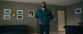 Movie still from “The Covenant” (2023), directed by Guy Ritchie – A man standing in front of a painting in a living room; Medium shot, Low angle