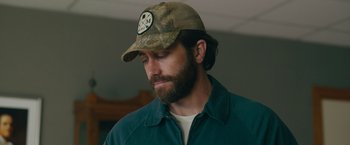 Movie still from “The Covenant” (2023), directed by Guy Ritchie – A man with a beard wearing a baseball cap; Close Up shot, Over the shoulder angle