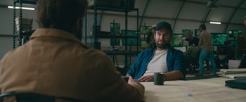 Movie still from “The Covenant” (2023), directed by Guy Ritchie – Two men are sitting at a table and one of them is holding a coffee mug; Medium shot, Over the shoulder angle