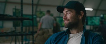 Movie still from “The Covenant” (2023), directed by Guy Ritchie – A man with a beard wearing a baseball cap; Close Up shot, Over the shoulder angle