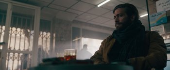 Movie still from “The Covenant” (2023), directed by Guy Ritchie – A man sitting at a table with a drink in front of him; Medium shot, Low angle
