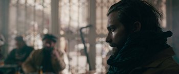 Movie still from “The Covenant” (2023), directed by Guy Ritchie – A man with long hair and a goatee looking to his left; Close Up shot, Over the shoulder angle