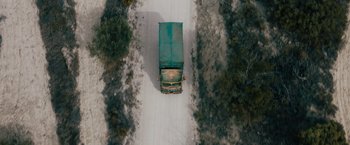 Movie still from “The Covenant” (2023), directed by Guy Ritchie – An aerial view of a truck driving down the road; Extreme Wide shot, Overhead angle