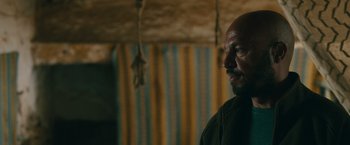 Movie still from “The Covenant” (2023), directed by Guy Ritchie – A man with a bald head is standing in a room; Close Up shot, Over the shoulder angle