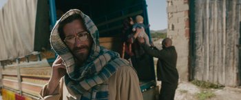 Movie still from “The Covenant” (2023), directed by Guy Ritchie – A man with a beard wearing a scarf and glasses; Medium shot, Low angle