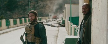 Movie still from “The Covenant” (2023), directed by Guy Ritchie – A man in a military uniform standing in front of a building; Medium shot, Over the shoulder angle