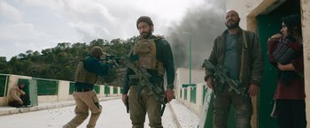 Movie still from “The Covenant” (2023), directed by Guy Ritchie – A man with a gun and a rifle on a bridge; Medium shot, Low angle