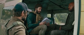 Movie still from “The Covenant” (2023), directed by Guy Ritchie – A man sitting in a vehicle reading a book; Medium shot, Over the shoulder angle