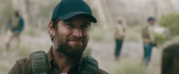 Movie still from “The Covenant” (2023), directed by Guy Ritchie – A person with a beard wearing a hat; Close Up shot, Over the shoulder angle