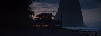 Movie still from “The Creator” (2023), directed by Gareth Edwards – A house on the beach at night with a mountain in the background; Extreme Wide shot, Low angle