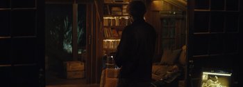 Movie still from “The Creator” (2023), directed by Gareth Edwards – A man standing in front of a book shelf; Medium shot, Over the shoulder angle