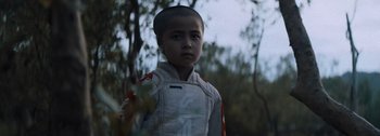 Movie still from “The Creator” (2023), directed by Gareth Edwards – A young boy in a spacesuit standing next to a tree; Close Up shot, Low angle