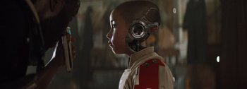 Movie still from “The Creator” (2023), directed by Gareth Edwards – A young boy wearing a helmet with headphones on his head; Close Up shot, Over the shoulder angle