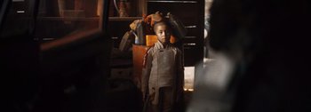 Movie still from “The Creator” (2023), directed by Gareth Edwards – A young boy in a uniform standing in a room; Medium shot, Over the shoulder angle