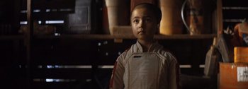 Movie still from “The Creator” (2023), directed by Gareth Edwards – A young boy wearing a bib stands in front of a shelf; Close Up shot, Over the shoulder angle