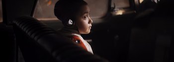 Movie still from “The Creator” (2023), directed by Gareth Edwards – A young boy wearing a helmet and ear muffs; Close Up shot, Over the shoulder angle