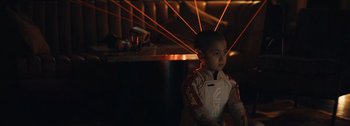 Movie still from “The Creator” (2023), directed by Gareth Edwards – A young boy is standing in a dark room; Medium shot, Over the shoulder angle