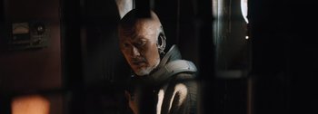Movie still from “The Creator” (2023), directed by Gareth Edwards – A man with a bald head wearing a helmet; Close Up shot, Over the shoulder angle
