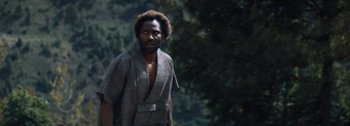Movie still from “The Creator” (2023), directed by Gareth Edwards – A man in a bathrobe standing in a wooded area; Close Up shot, Low angle
