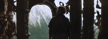 Movie still from “The Creator” (2023), directed by Gareth Edwards – A man standing in front of an archway with mountains in the background; Medium shot, Over the shoulder angle