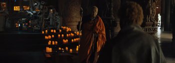 Movie still from “The Creator” (2023), directed by Gareth Edwards – A monk holding a staff in front of candles in a temple; Medium shot, Over the shoulder angle