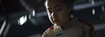 Movie still from “The Creator” (2023), directed by Gareth Edwards – A young girl wearing a white shirt and a red and white jacket; Close Up shot, Low angle