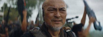 Movie still from “The Creator” (2023), directed by Gareth Edwards – An older man with a gray beard is holding a cell phone; Close Up shot, Over the shoulder angle