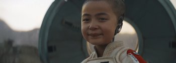 Movie still from “The Creator” (2023), directed by Gareth Edwards – A young boy with a headset in his ears; Close Up shot, Over the shoulder angle