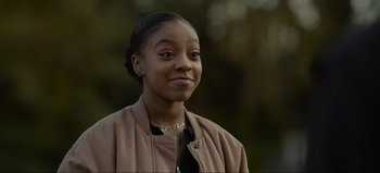 Movie still from “The Curse of Bridge Hollow” (2022), directed by Jeff Wadlow – A young woman wearing a brown jacket and smiling for the camera; Close Up shot, Over the shoulder angle