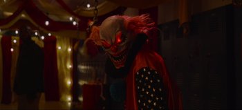 Movie still from “The Curse of Bridge Hollow” (2022), directed by Jeff Wadlow – A creepy clown with red eyes and a red hair wig; Medium shot, Over the shoulder angle