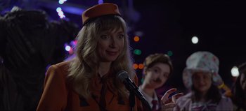Movie still from “The Curse of Bridge Hollow” (2022), directed by Jeff Wadlow – A woman wearing an orange hat is speaking into a microphone; Close Up shot, Over the shoulder angle