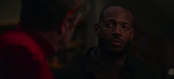 Movie still from “The Curse of Bridge Hollow” (2022), directed by Jeff Wadlow – A man in a dark room with another man in the background; Close Up shot, Over the shoulder angle