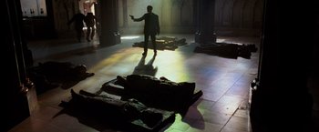 Movie still from “The Da Vinci Code” (2006), directed by Ron Howard – A man holding a gun while standing in a room; Wide shot, High angle