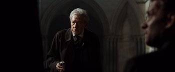 Movie still from “The Da Vinci Code” (2006), directed by Ron Howard – An older man in a suit and tie holding a gun; Medium shot, Low angle